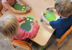 dzieci siedzą przy stolikach i układają żaby z kół origami