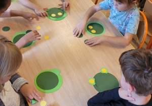 dzieci siedzą przy stolikach i układają żaby z kół origami