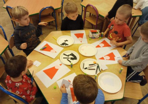 Dzieci przy stoliku wykonują pracę plastyczną.