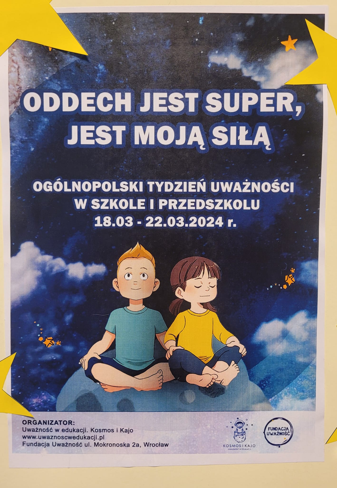 Plakat tygodnia uważności a na nim dwójka dzieci siedząca i medytująca. 