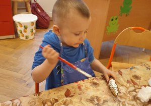 Chłopiec maluje białą farbą szyszkę