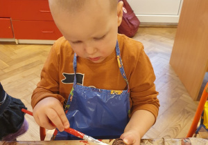 Chłopiec maluje białą farbą szyszkę