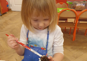 Dziewczynka maluje farbą szyszkę