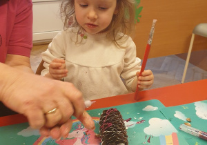 Dziewczynka maluje szyszkę brokatem