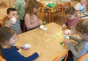 Dzieci doklejają wycięte wcześniej kolorowe kwiaty.