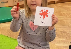 dziewczynka prezentująca kartę obrazkową z kolorem "red" oraz czerwoną kredkę