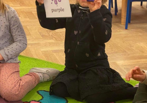 dziewczynka prezentująca kartę obrazkową z kolorem "purple" oraz fioletowy klocek
