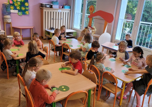 dzieci siedzą przy stolikach i układają żaby z kół origami