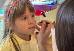 nauczycielka maluje dziewczynce kropki na policzkach