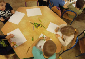 Dzieci przy stoliku rysują kredkami.